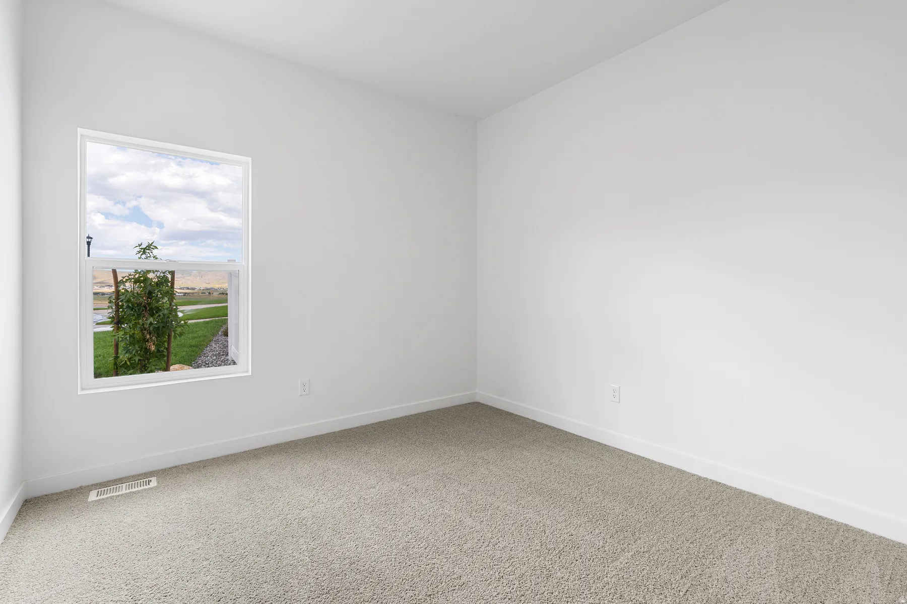 Bright corner bedroom with expansive window framing scenic countryside vistas, neutral carpet flooring, and clean white walls providing a serene retreat