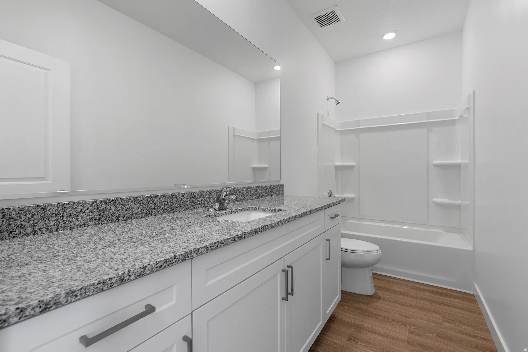Spa-inspired bathroom featuring a granite speckled countertop with dual sink vanity, white cabinetry with brushed metal hardware, and a walk-in shower with frameless glass enclosure and built-in shelving