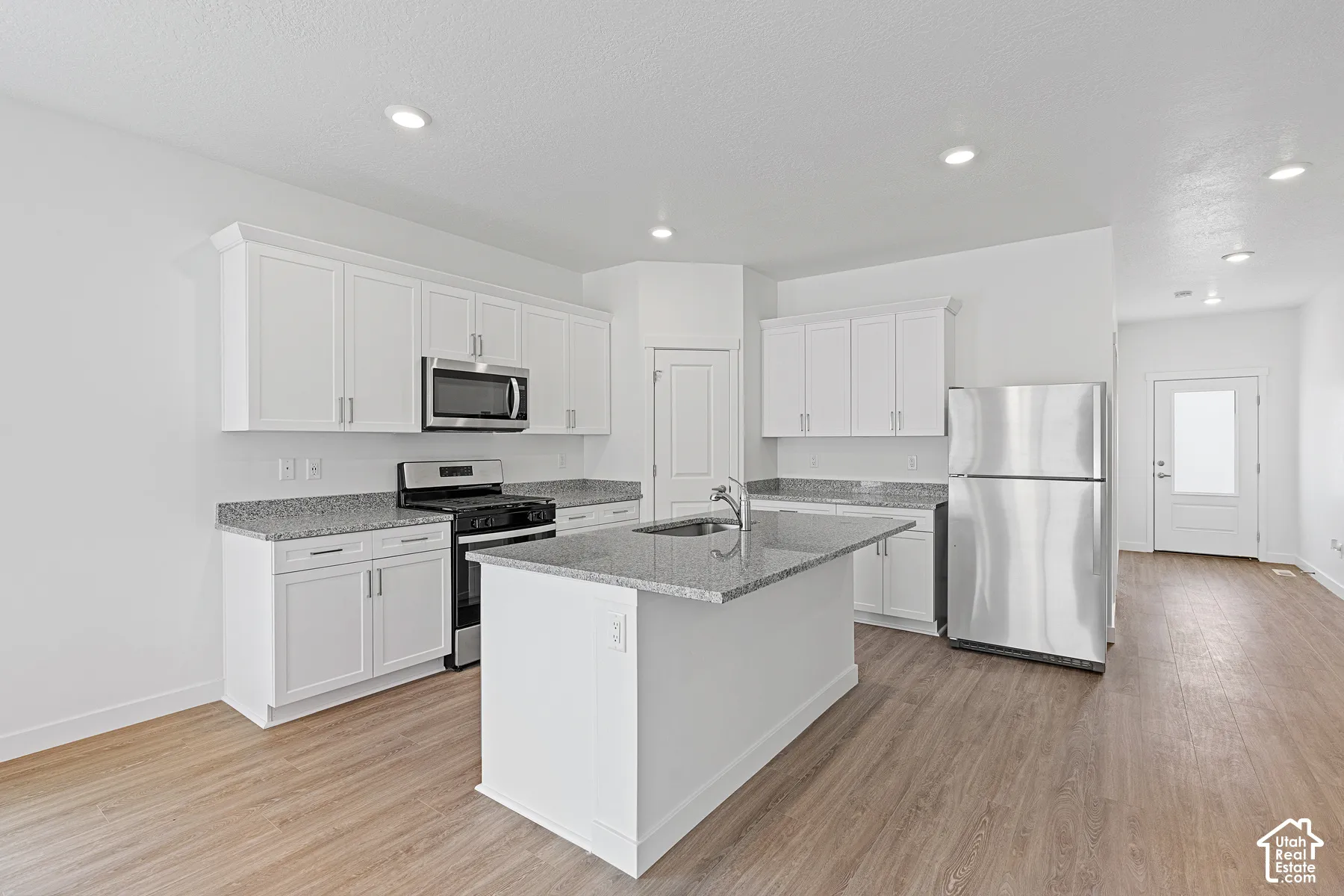Modern kitchen featuring white cabinetry, stainless steel appliances including a microwave and refrigerator, gray quartz countertops, a center island with additional storage, recessed lighting, and wood-finish flooring throughout the open layout