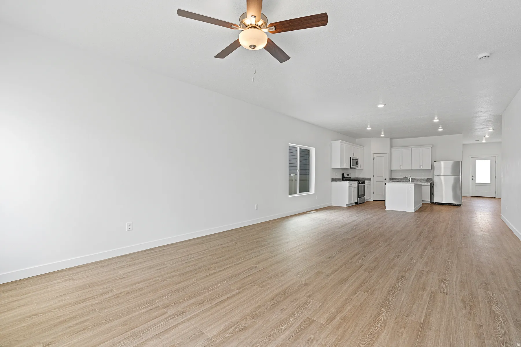 Spacious open-concept living area featuring wood-finish flooring throughout, recessed ceiling lighting, and a ceiling fan with integrated light fixture
