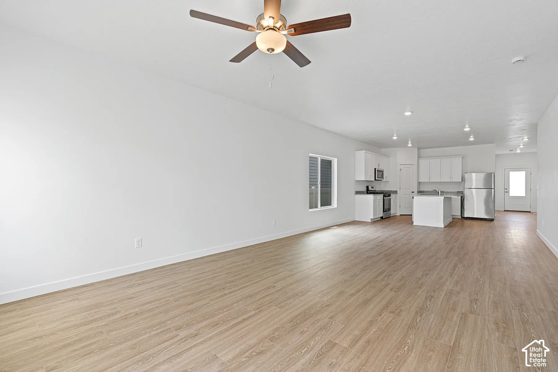 Spacious open-concept living area featuring wood-finish flooring throughout, recessed ceiling lighting, and a ceiling fan with integrated light fixture