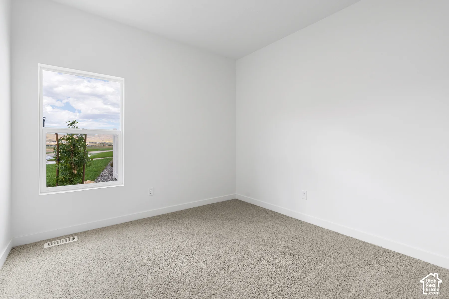 Bright corner bedroom with expansive window framing scenic countryside vistas, neutral carpet flooring, and clean white walls providing a serene retreat