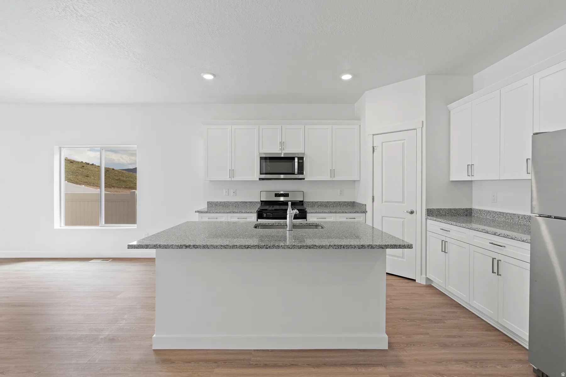 Open-concept kitchen featuring an island with a sink, white cabinetry, integrated stainless steel appliances, granite-style countertops, and wood-finish flooring