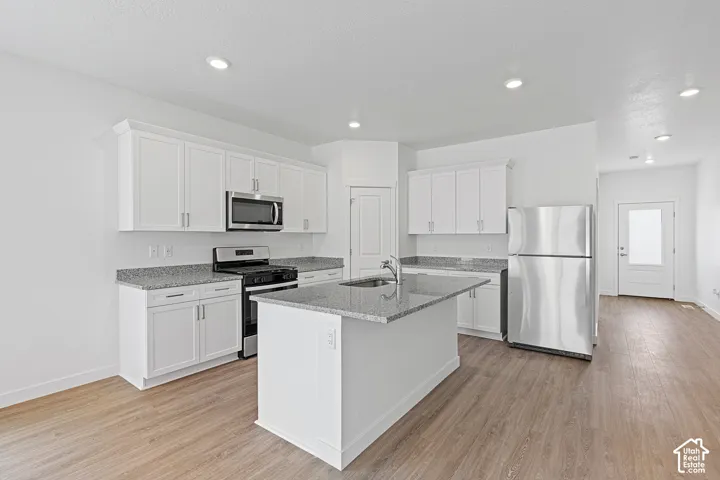 Modern kitchen featuring white cabinetry, stainless steel appliances including a microwave and refrigerator, gray quartz countertops, a center island with additional storage, recessed lighting, and wood-finish flooring throughout the open layout