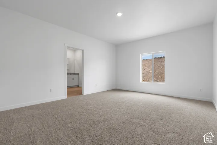 Spacious bedroom showcasing neutral carpeting, abundant natural light from a large window, recessed ceiling lighting, and direct access to an ensuite bathroom with glass-enclosed shower