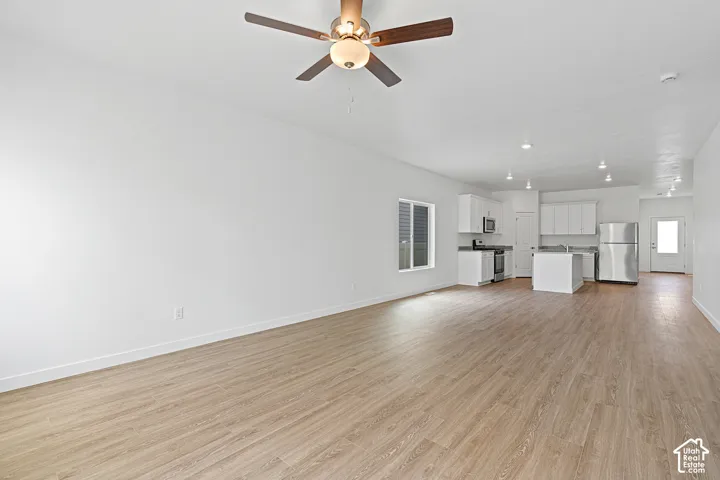 Spacious open-concept living area featuring wood-finish flooring throughout, recessed ceiling lighting, and a ceiling fan with integrated light fixture