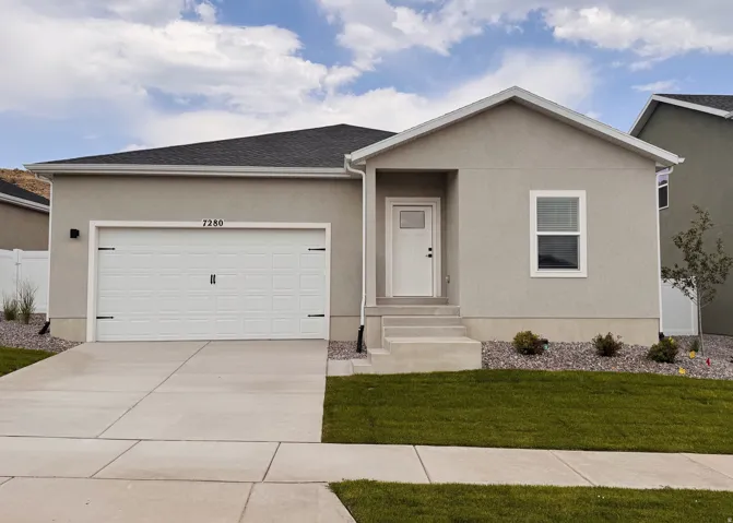 Contemporary ranch-style home featuring a clean stucco exterior in neutral tones, white two-car garage with paneled doors, manicured front lawn with decorative rock landscaping, concrete driveway and walkway, and a covered entry portico with single-panel