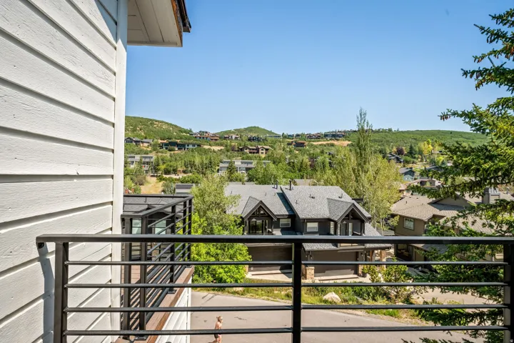 Elevated deck with horizontal metal railings overlooking manicured grounds, mature landscaping, and rolling hillside terrain