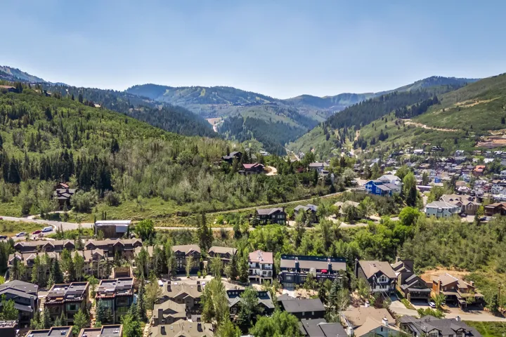 Nestled in a verdant mountain valley, this aerial perspective showcases a residential community surrounded by dense evergreen forests and rolling alpine terrain