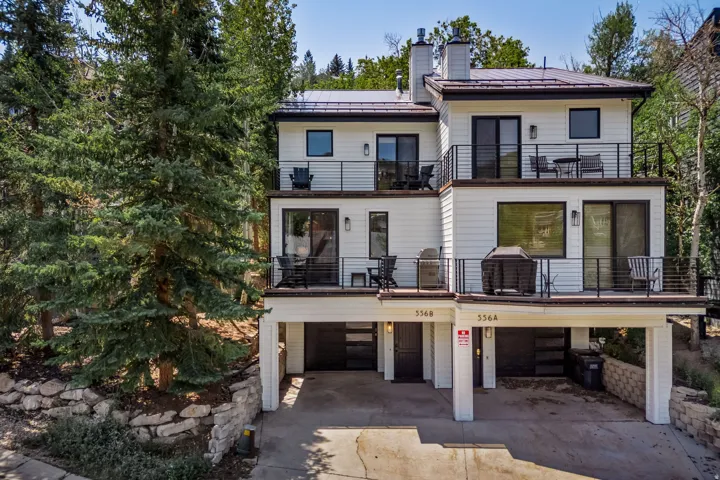 Contemporary multi-story exterior with white siding, multiple balconies with black railings, and a dark metal roof