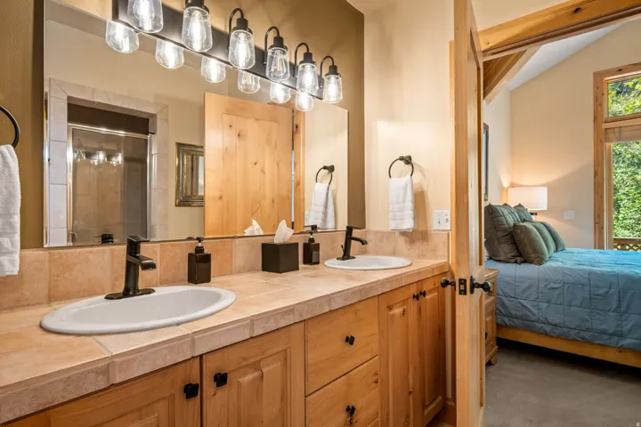 Dual basin vanity with tiled countertop, natural wood cabinetry, and matte black fixtures