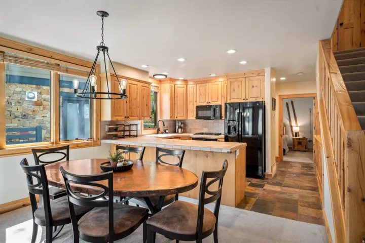 Warm wood cabinetry and beamed ceiling details frame this open kitchen and dining area, featuring black appliances, a centered island with prep space, pendant lighting, and a round dining table with seating for four
