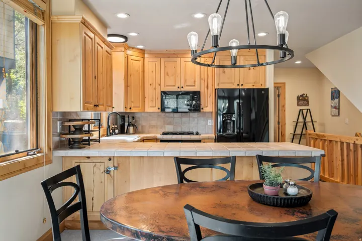 Kitchen featuring wood cabinetry, black appliances, tile backsplash, tile countertops, and a black chandelier