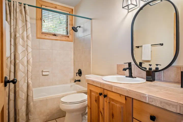 Wood-finish vanity with an integrated sink, tile countertop, and oval mirror