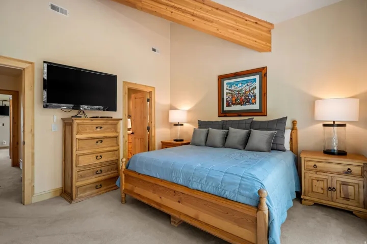 Vaulted ceiling with exposed wood beams, wall-mounted television, wood-trim doorway, and carpeted flooring