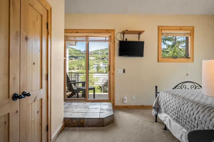 Wooden door with black hardware, sliding glass door leading to an outdoor deck, natural wood window trim, mounted television, and carpeting