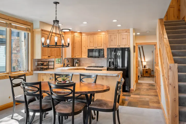 Kitchen and dining area featuring natural wood cabinetry, black appliances, a tile backsplash, and a staircase with carpeted treads