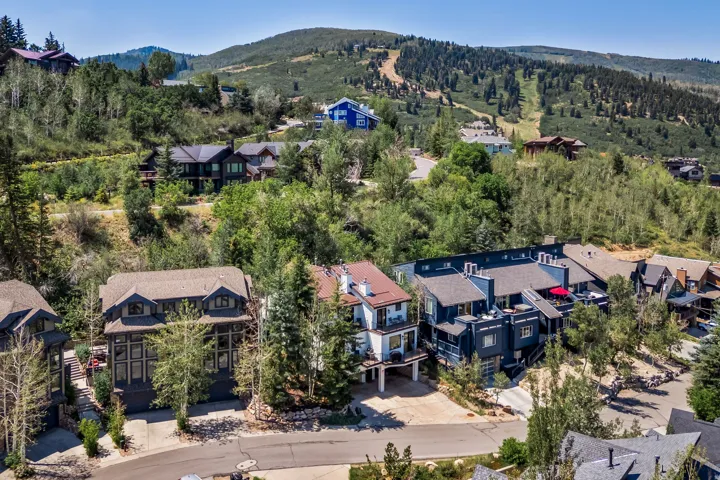 Hillside contemporary estate nestled among mature coniferous trees, featuring modern architectural design with dark exterior siding, multi-level construction, and expansive grounds set within a forested residential community with mountain backdrop