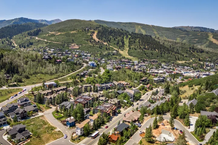 Aerial perspective of a residential community nestled within forested mountain terrain, featuring tree-lined streets, multi-unit residential structures, and sloped topography with mature coniferous and deciduous vegetation throughout the neighborhood