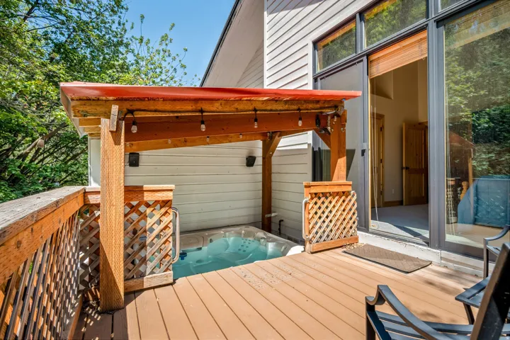 Expansive composite deck with composite decking and integrated hot tub featuring wooden pergola with overhead lighting