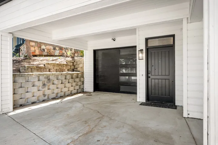 Spacious garage featuring concrete flooring, black overhead sectional door with glass panels, black entry door with multi-panel design, and white beam ceiling structure