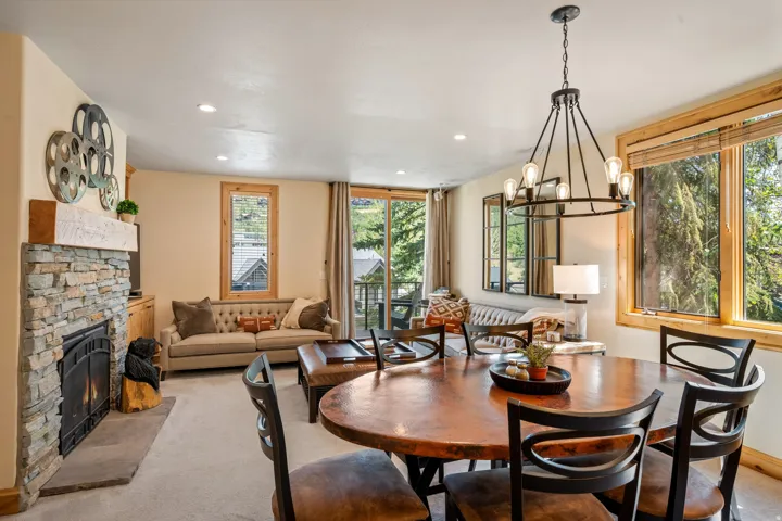 Open-concept living and dining area featuring a wood-finish round dining table, black ladder-back chairs, and a stone fireplace with metal detailing