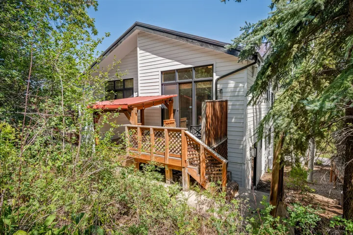 Wood deck with lattice railing, covered by a wood pergola with a red roof, leading to a home with horizontal siding and dark-trimmed windows