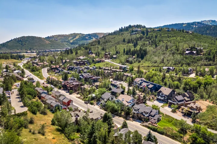 Aerial perspective of this hillside community showcasing custom residences nestled among mature evergreen and deciduous trees, with winding streets, varied architectural styles, and abundant natural landscaping across multiple elevations against a backdro