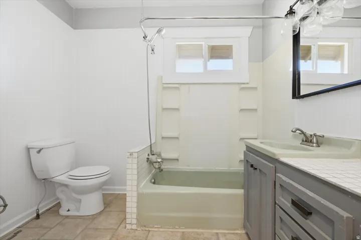 Bathroom featuring a bathtub with shower fixture, a single vanity with an integrated sink, a mirror, and tiled flooring