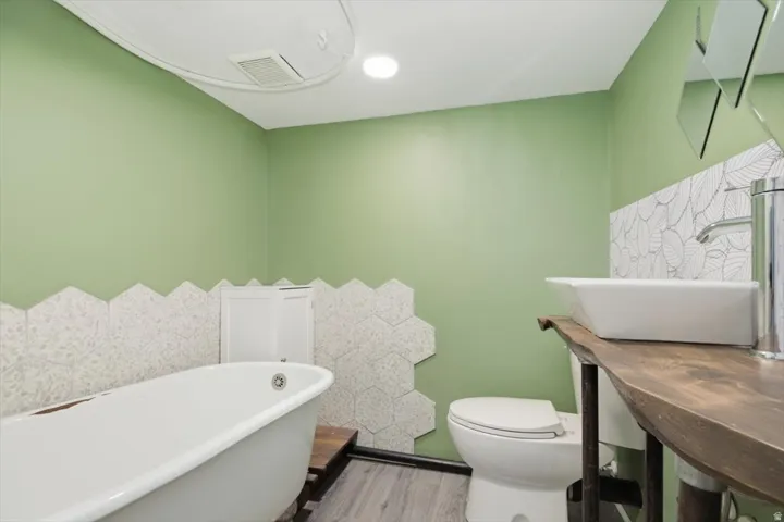 Freestanding bathtub, wood-finish flooring, hexagon wall tile, white vessel sink, and a wood vanity