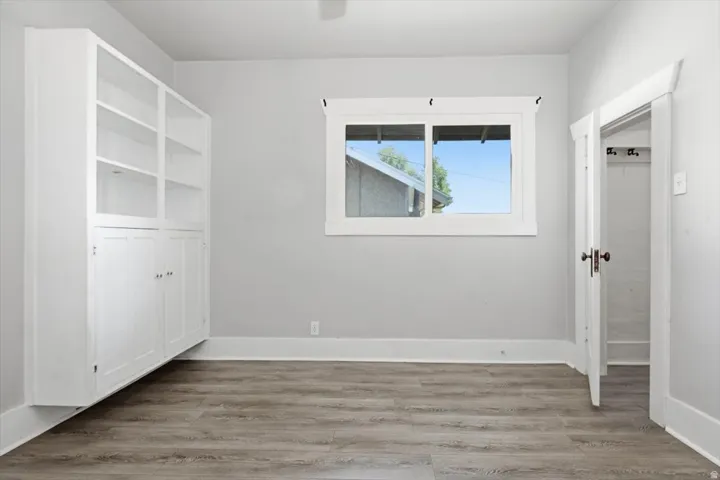 Bright and spacious room featuring hardwood-finish flooring, large dual-pane windows with natural light, custom white built-in cabinetry with shelving, and clean white walls throughout