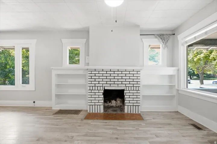 Built-in shelving, wood-finish flooring, white brick fireplace, multiple windows, ceiling light fixture