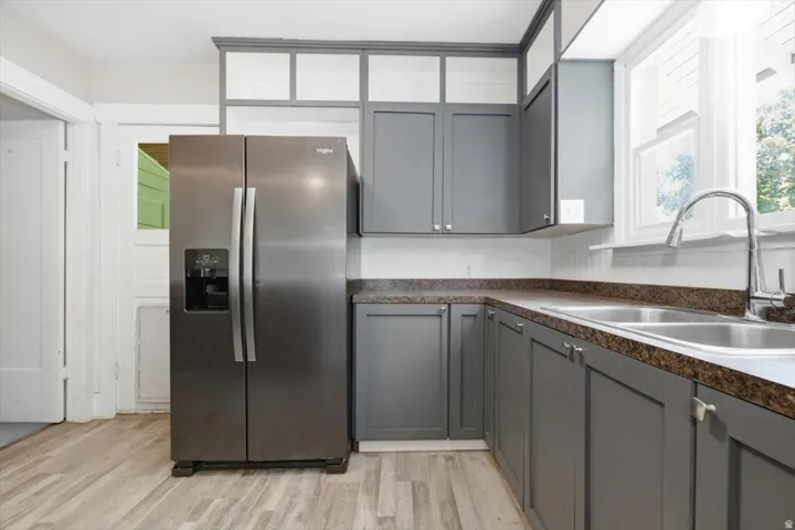 Modern kitchen featuring stainless steel side-by-side refrigerator, gray cabinetry with brushed metal hardware, granite countertops, undermount sink with contemporary faucet, and wood-finish flooring throughout