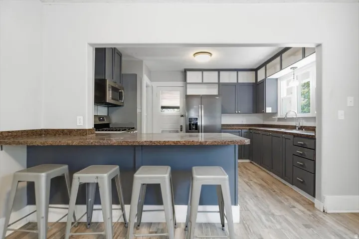 Kitchen featuring stainless steel appliances, wood-finish flooring, a breakfast bar, gray cabinetry, and a window over the sink