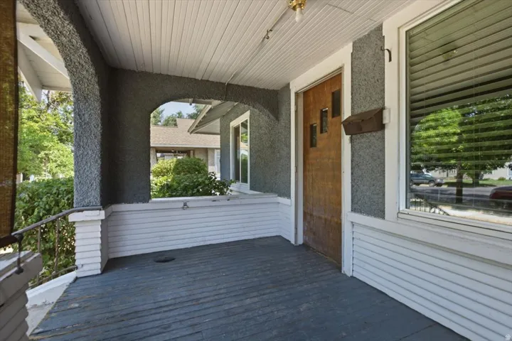 Covered front porch featuring white horizontal siding, dark composite flooring, white beadboard ceiling with recessed lighting, and stone-clad support columns