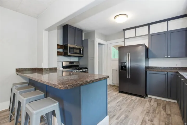 Kitchen featuring a built-in breakfast bar, wood-finish flooring, dark cabinetry, and stainless steel appliances