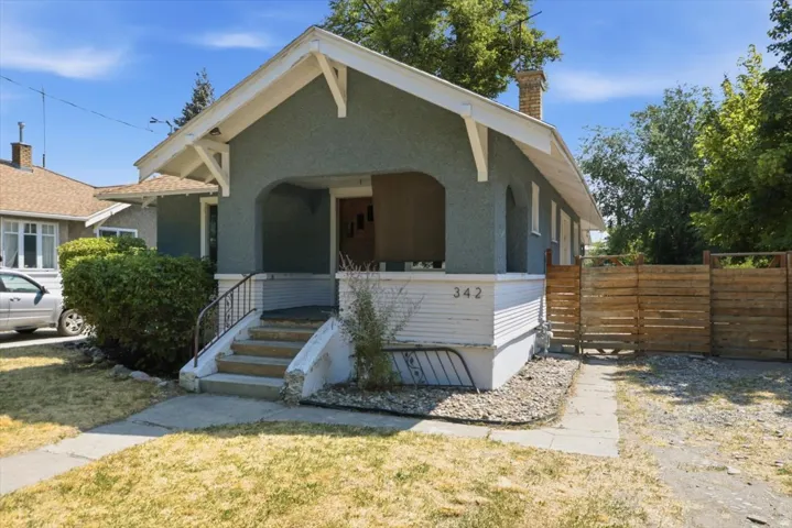 Stucco exterior with a covered porch, stone chimney, and a wooden privacy fence