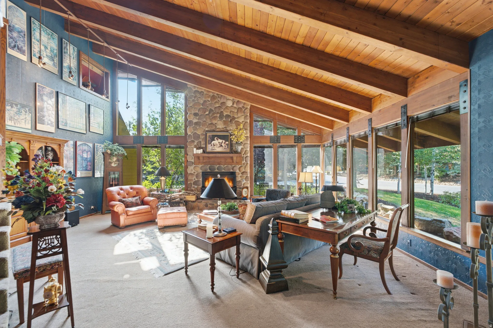 Vaulted wood-paneled ceiling with exposed beams, floor-to-ceiling windows, stone-clad fireplace, and full-height stone accent wall