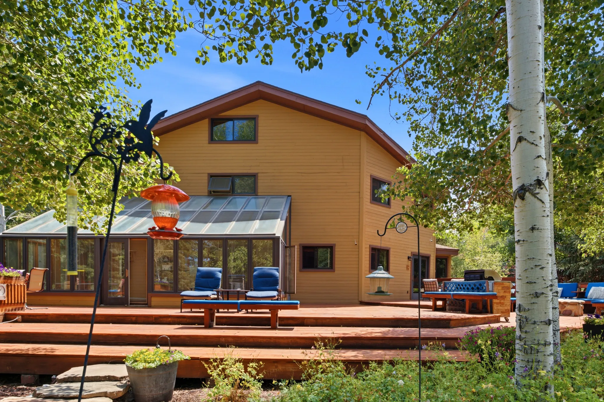 Expansive multi-level wood deck, glass-enclosed sunroom, and mature trees surrounding the property