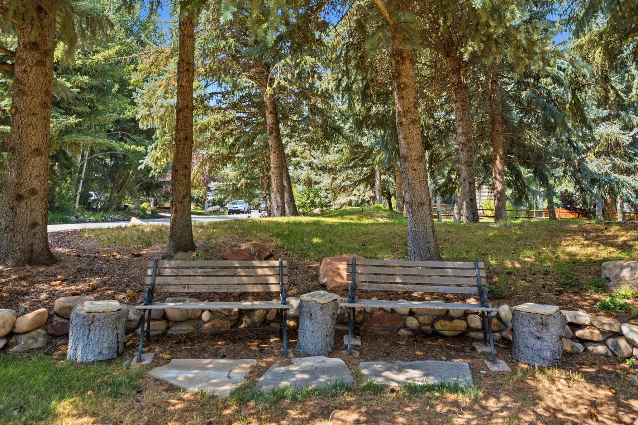 Mature trees, natural stone hardscaping, two wood benches with metal frames, and stepping stones