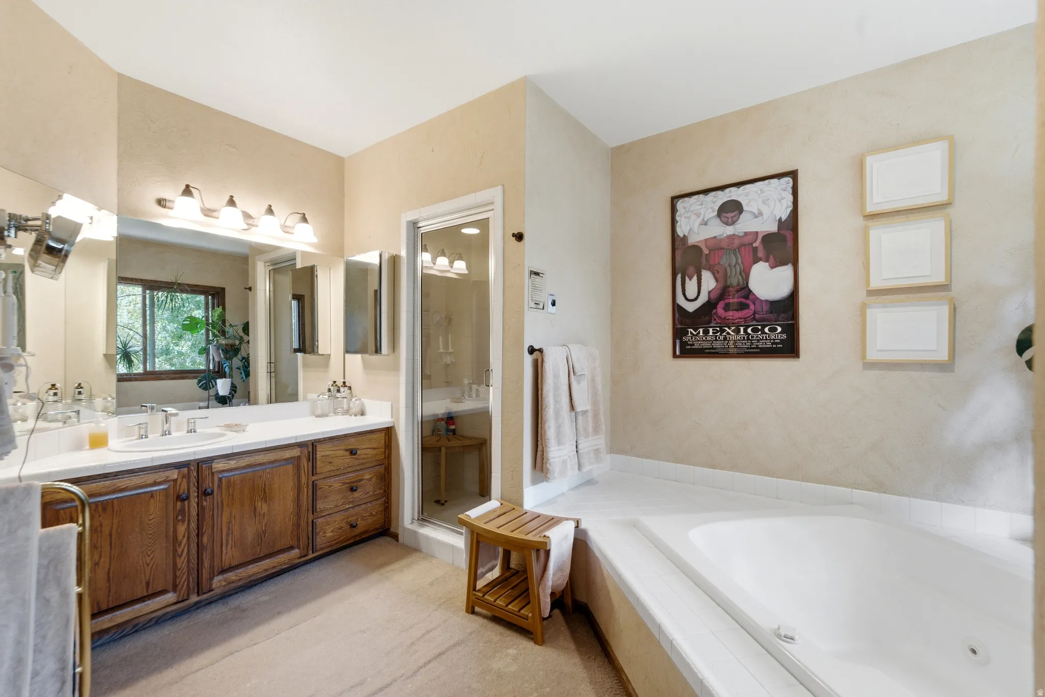 Primary with dual-sink vanity with wood-finish cabinetry, built-in soaking tub, glass-enclosed shower, and large wall-mounted mirror