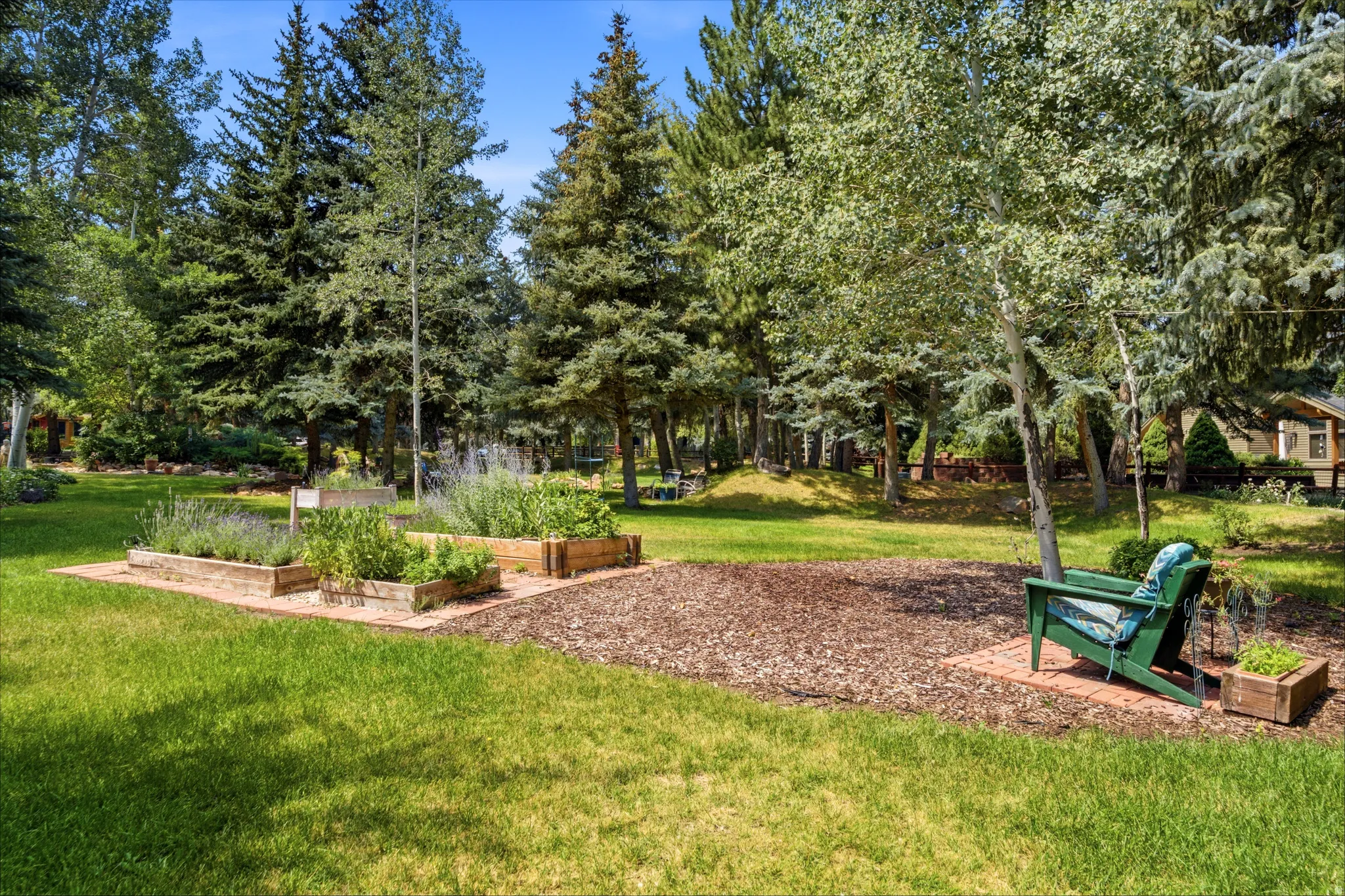 Expansive lawn area featuring multiple raised garden beds, mature trees, and a brick paver patio