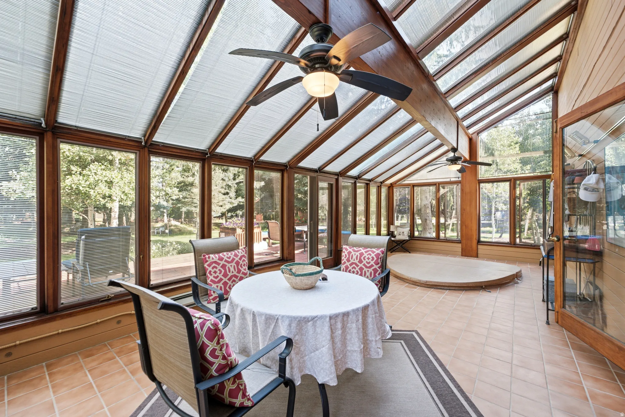 Sunroom featuring a vaulted glass ceiling with integrated blinds, wood-frame windows, ceiling fans, and tiled flooring