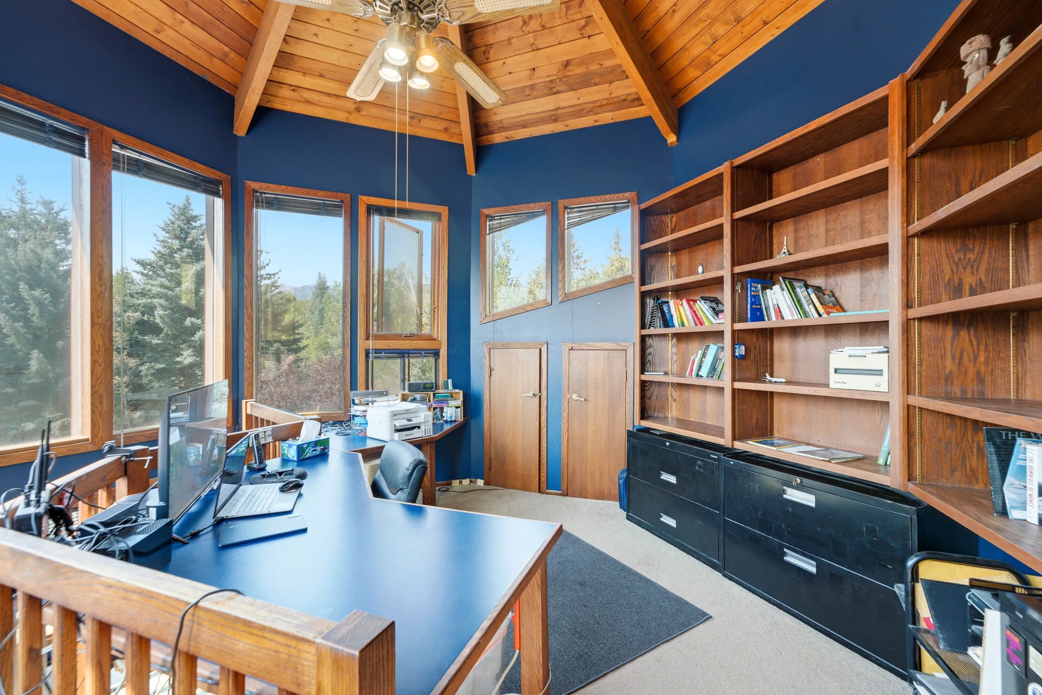 Crows Nest - Vaulted wood-finish ceiling, exposed wood-finish beams, integrated ceiling fan, multiple wood-framed windows, and built-in wood-finish shelving