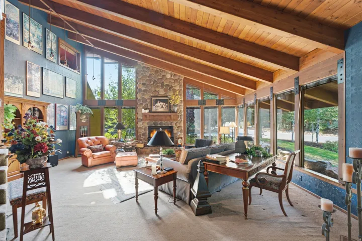 Vaulted wood-paneled ceiling with exposed beams, floor-to-ceiling windows, stone-clad fireplace, and full-height stone accent wall
