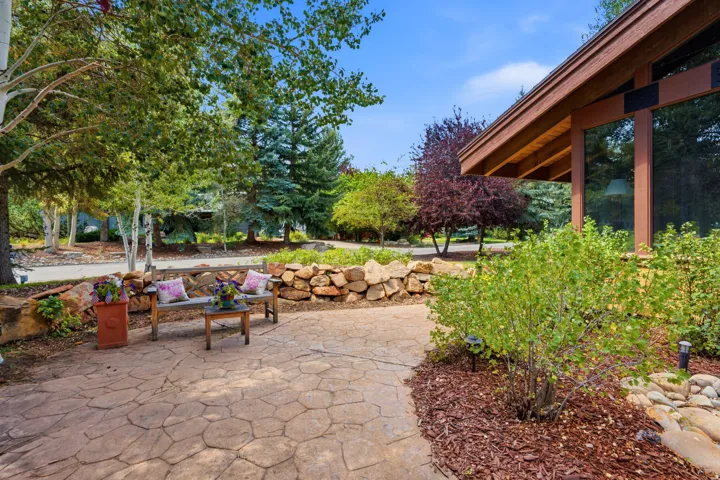Stone paver patio with a stone retaining wall, surrounded by mature trees and shrubs