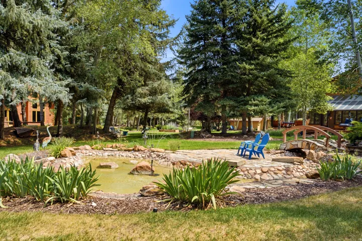 Expansive outdoor area featuring a stone-lined pond, flagstone patio, and a decorative wooden bridge