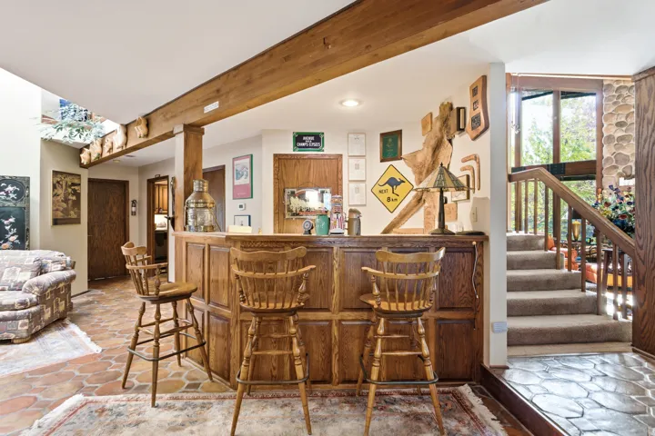 Welcoming entry featuring exposed wooden beam ceiling, custom wood cabinetry with seated bar seating, terra cotta tile flooring, and abundant natural light from multiple windows