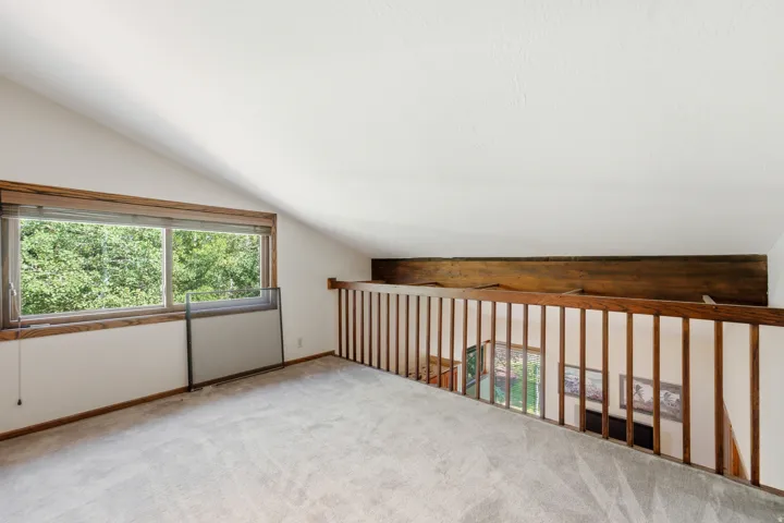 loft - Carpeted loft space with a vaulted ceiling and a wood-framed window