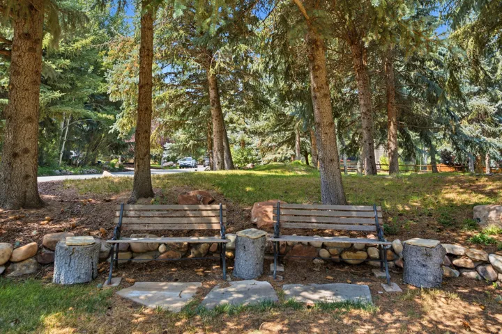Mature trees, natural stone hardscaping, two wood benches with metal frames, and stepping stones